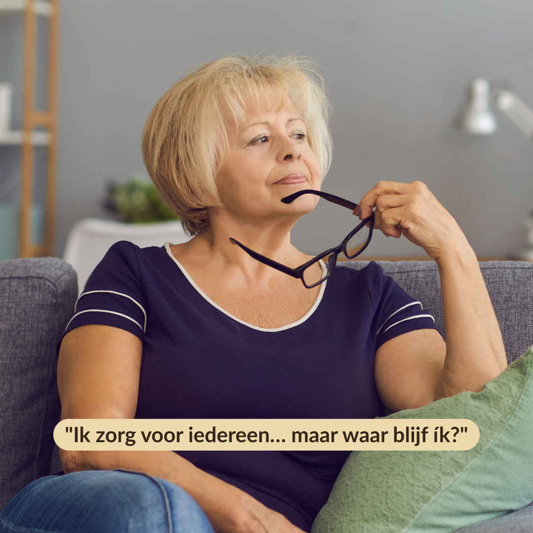 Vrouw van middelbare leeftijd zit peinzend op de bank met haar bril in de hand. Ze kijkt voor zich uit, alsof ze zich afvraagt: ‘Ik zorg voor iedereen… maar waar blijf ík?’
